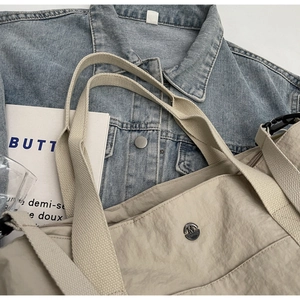 Close-up of beige nylon tote bag featuring metal M Fashion logo and durable fabric handle