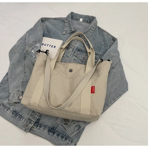 Detail view of the cream beige nylon tote bag showing double handles and fashion label