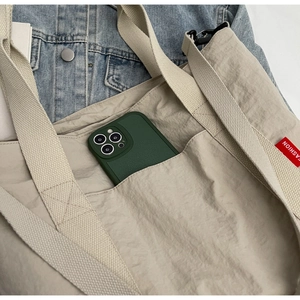Close-up of beige nylon tote bag showing front pocket with smartphone and fashion label