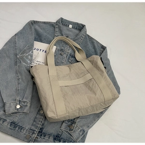 Close-up of beige nylon tote bag with pleated texture on blue denim background