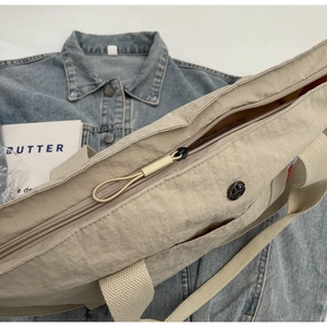 Detail of beige nylon tote bag featuring a round metal logo and smooth zipper closure