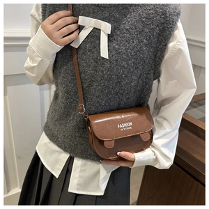 Detail of a brown vintage leather shoulder bag featuring buckled straps and printed text