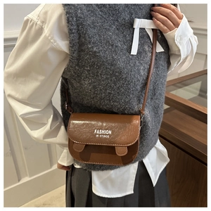 Brown glossy faux leather saddle bag with text strap detail shown on a model