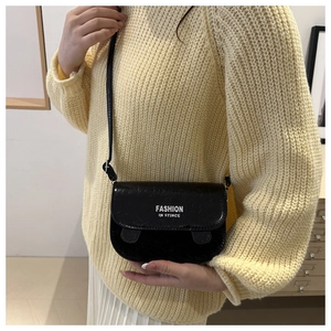 Detail of black patent leather crossbody bag with white fashion text and cat ear accents