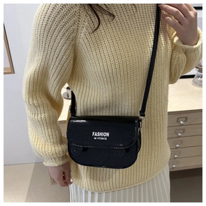 Close-up of a glossy black crossbody bag with 'FASHION IN STINCE' text on a yellow sweater