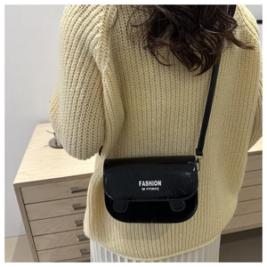 Detail of a black glossy crossbody bag with white fashion text on textured leather