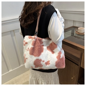 Close-up of fluffy cow print plush tote bag with pink leather strap in cozy setting