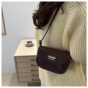 Detail of a small dark brown leather crossbody bag featuring white text on the front flap