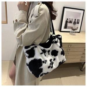 Detail of cow print plush shoulder bag with long black strap worn with a beige trench coat