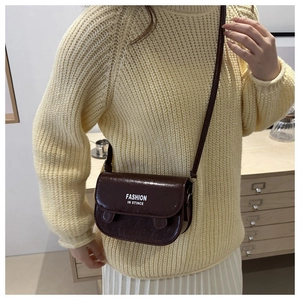 Brown mini crossbody bag with glossy texture worn over a yellow sweater and white skirt