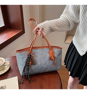 Detail of grey felt and brown leather tote bag with braided charm and metallic logo