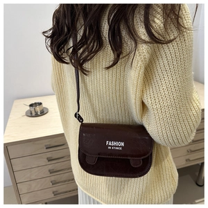 Detail of a dark brown glossy leather crossbody bag with white fashion print text