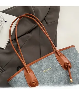Detail shot of grey textured tote bag with brown leather straps and gold lettering