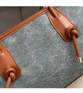 Detailed shot of grey textured fabric tote bag with orange leather handles and knot accents