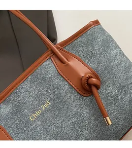 Detail of grey denim tote bag with brown leather trim and golden hardware accents