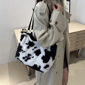 Fashionable cow print plush tote bag with black straps worn by a model in a beige trench coat