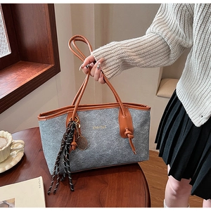 Detail of grey felt tote bag with brown leather handles and tennis racket charm