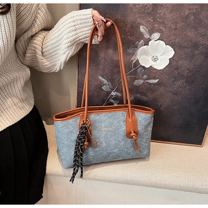 Detail of light blue felt tote bag with brown leather handles and decorative tassel