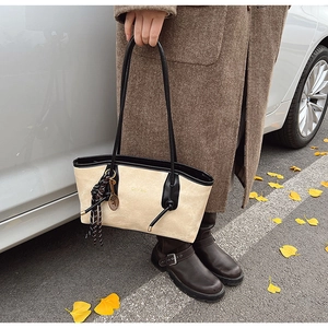 Detail of a beige tote bag with black trim and a tennis racket charm in autumn setting