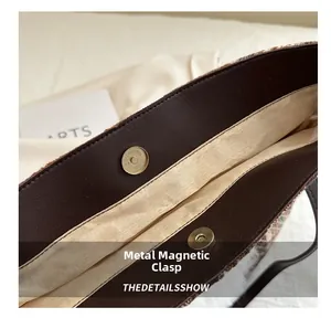Detail of metal magnetic buckles on textured tweed tote bag with brown leather trim