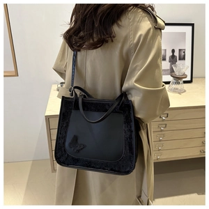 Chic black tote bag with plush fur trim and butterfly decor shown on a khaki trench coat