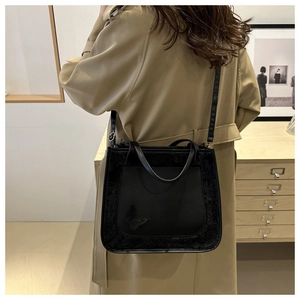 Detail view of black faux leather tote with butterfly appliqué shown on model shoulder