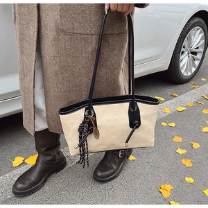 Detail of a large beige textured tote bag with black leather straps and gold logo accent