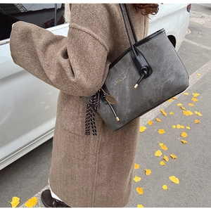 Detail view of grey textured tote bag with tennis racket charm and tassel on shoulder