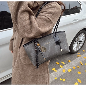 Detail of grey textured tote bag with black leather handles and tennis racket charm