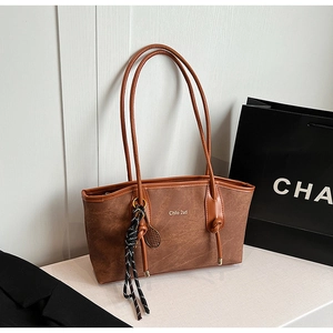 Detail of a brown textured faux leather tote bag with braided charm and long shoulder strap