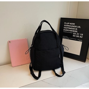 Détail du sac à dos en nylon noir avec poche latérale à cordon et étiquette tissée blanche