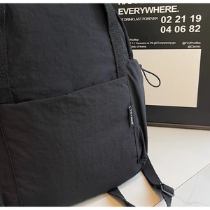 Gros plan sur le côté du sac à dos en nylon noir avec étiquette et cordon élastique