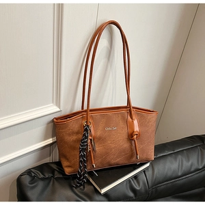 Detailed macro view of brown tote bag with metal logo and silk scarf on black leather sofa