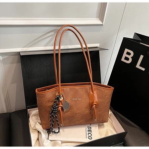 Close-up of brown textured leather tote bag with gold logo and tennis racket charm in gift box