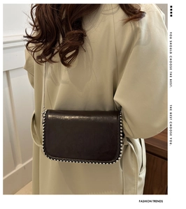 Detail of dark brown chain crossbody bag with silver rivet edges and faux leather texture
