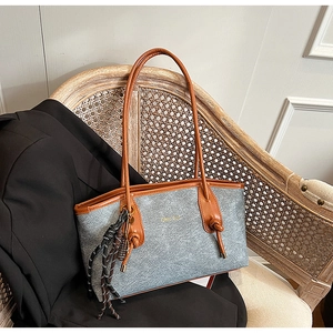 Detail of grey matte tote bag with brown leather handles and a woven tassel on a wooden chair