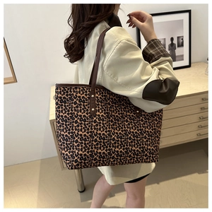 Detail of leopard print tote bag with brown leather strap worn by a model in a cozy setting