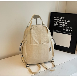 Détail du sac à dos crème montrant les poignées doubles et poches latérales à cordon