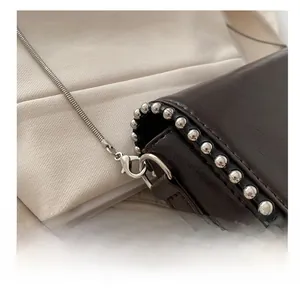 Macro detail of brown leather bag featuring silver rivets, metal chain, and lobster clasp