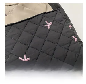 Détail du tissu en nylon matelassé noir avec motifs de nœuds roses brodés pour sac à main femme