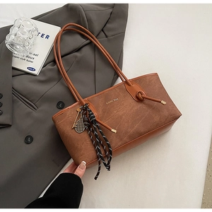 Close-up of brown textured tote bag featuring gold tennis racket charm and metal logo