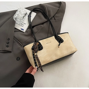Detail shot of beige suede tote bag with black leather straps and woven cord charm