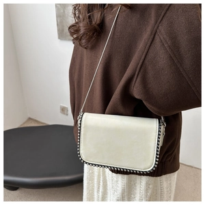 Detail of off-white crossbody bag with silver rivet edges and a metal chain strap