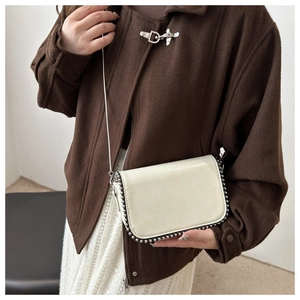 Close-up of a cream chain square bag featuring silver beaded metal trim on the edges