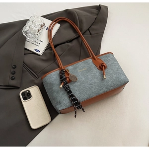 Detail of grey wool and brown leather tote bag with stylish knot charm on white desk