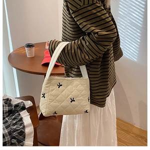 Vue latérale d'un sac cabas matelassé crème avec des nœuds noirs sur un mannequin