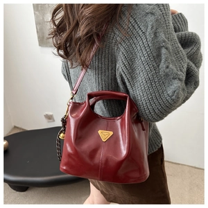 Detail view of burgundy leather bucket bag with gold triangle logo and tassel on model
