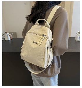Detail view of the cream nylon backpack showing the durable fabric and zipper strap pullers