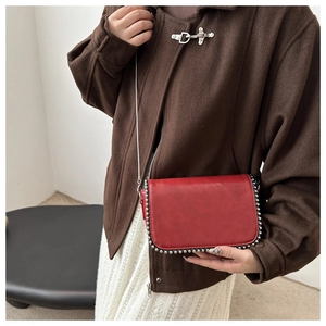 Close-up of red crossbody bag featuring silver rivet trim and a metallic chain strap
