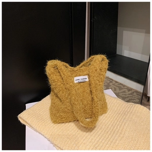 Gros plan sur un sac cabas en peluche jaune moutarde avec une étiquette de mode tissée